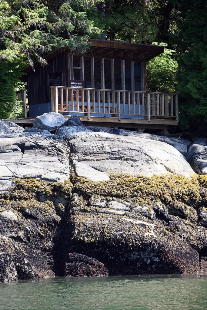The Weewanie Hot Springs perched on rocky shoreline surrounded by coastal forest near the Douglas Channel.
