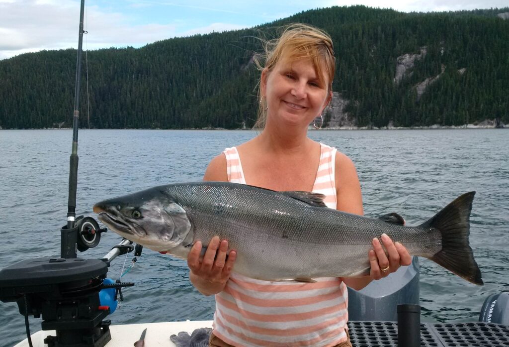 Woman holding a freshly caught salmon on a Kitimat fishing charter, Douglas Channel, BC.