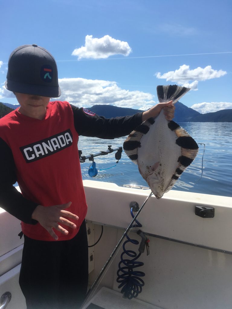 Young boy in a red Canada shirt proudly holding a sole on the deck of a fishing boat